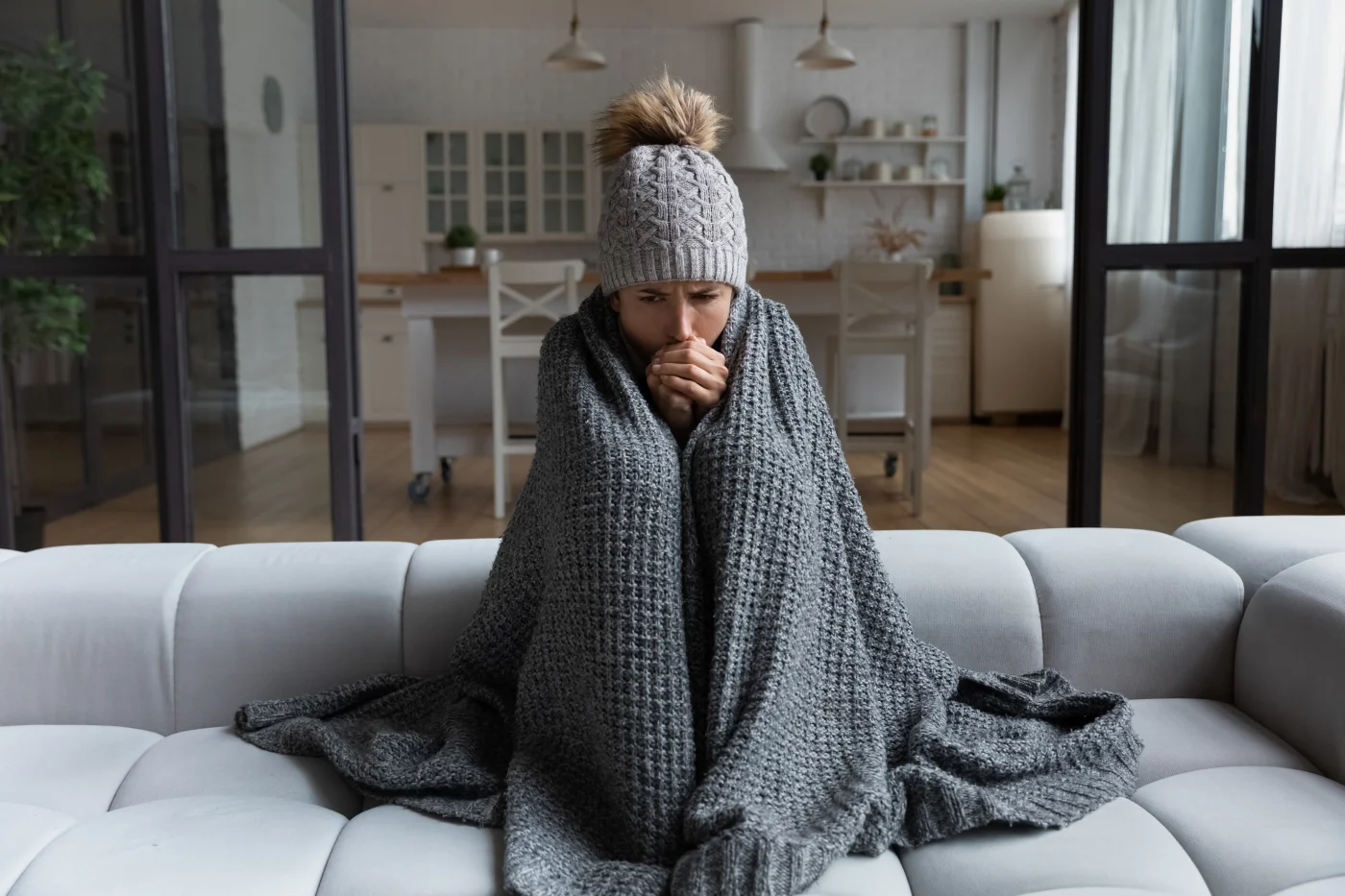 Twin Cities East Metro resident sits on couch with blanket and hat for warmth