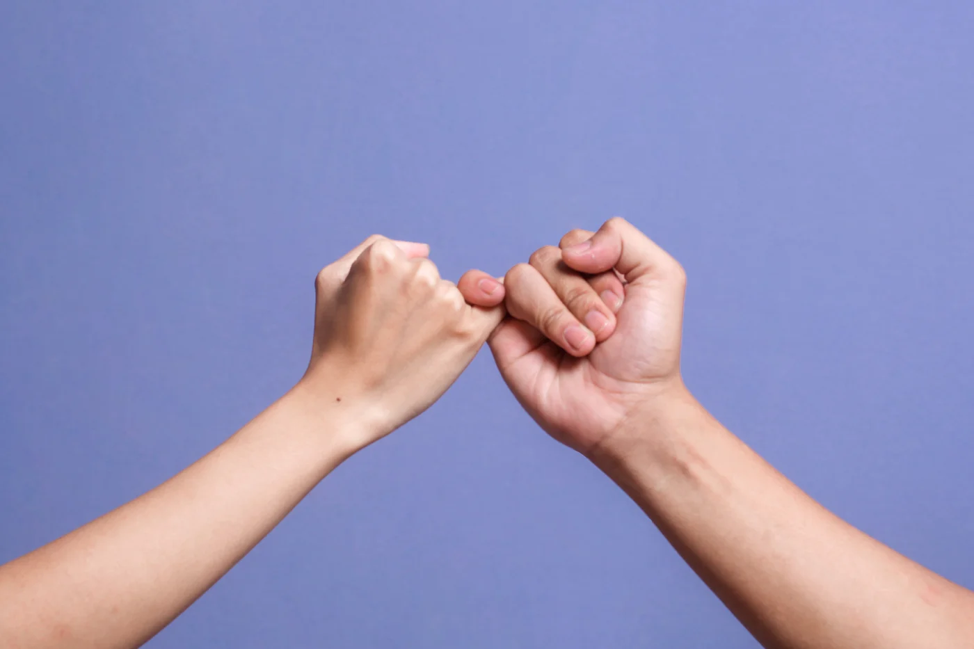 Two hands make a pinky promise in front of blue background