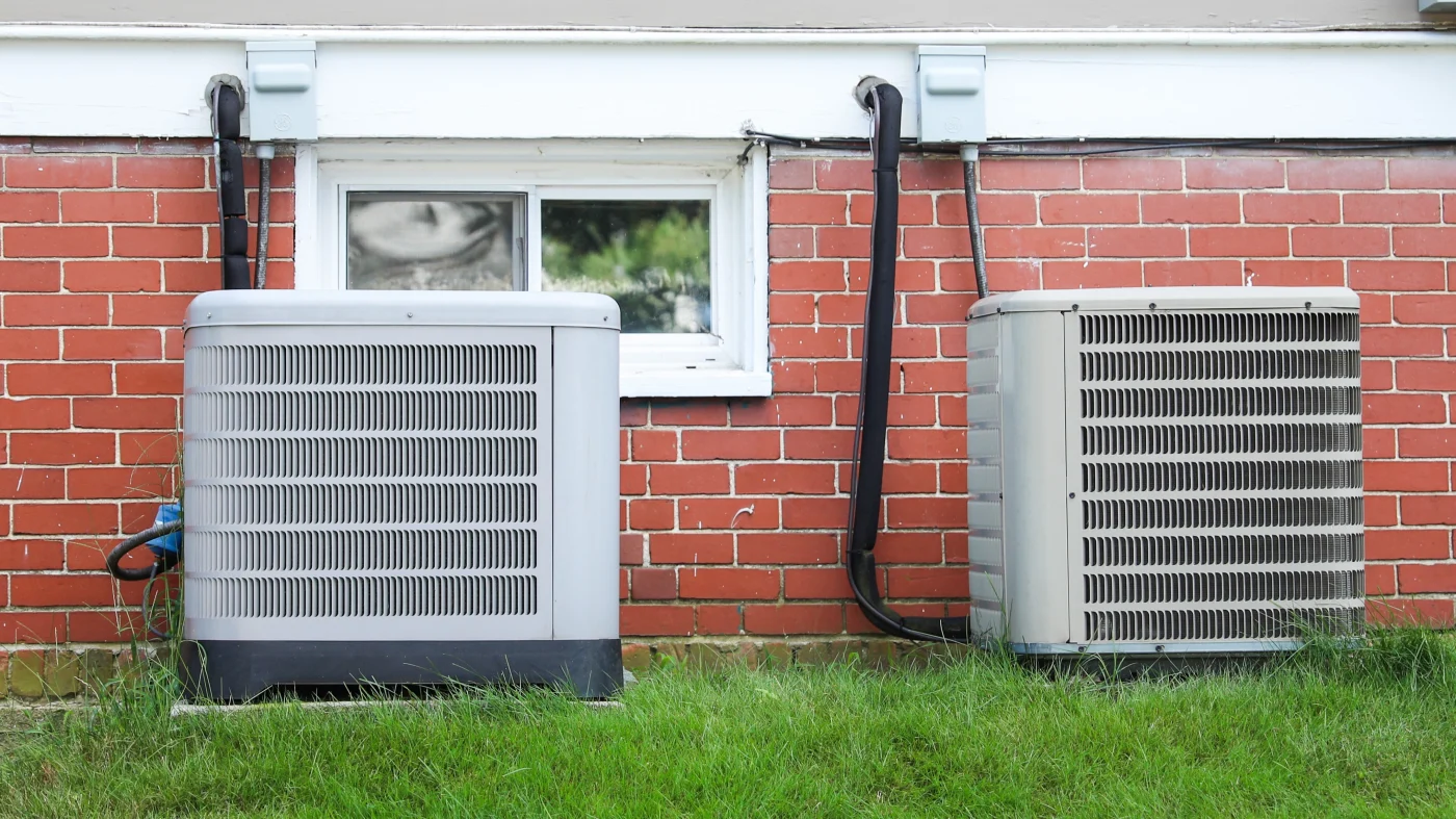 Two AC units outside of a home with brick siding.