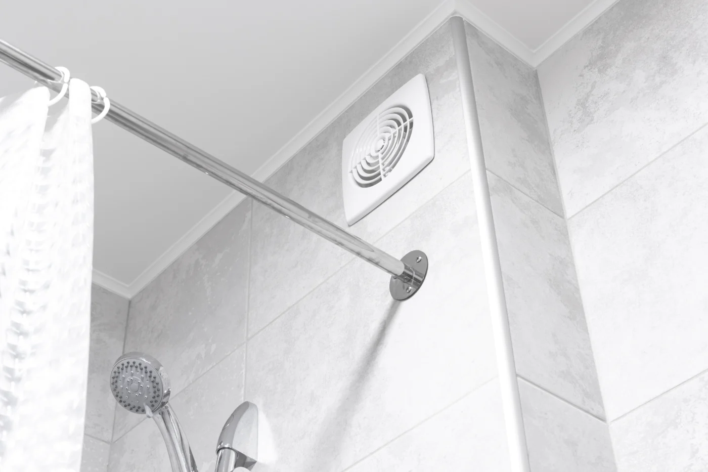 A white vent is shown above a bathtub/shower combo. The bathtub/shower has grey squares on the wall.