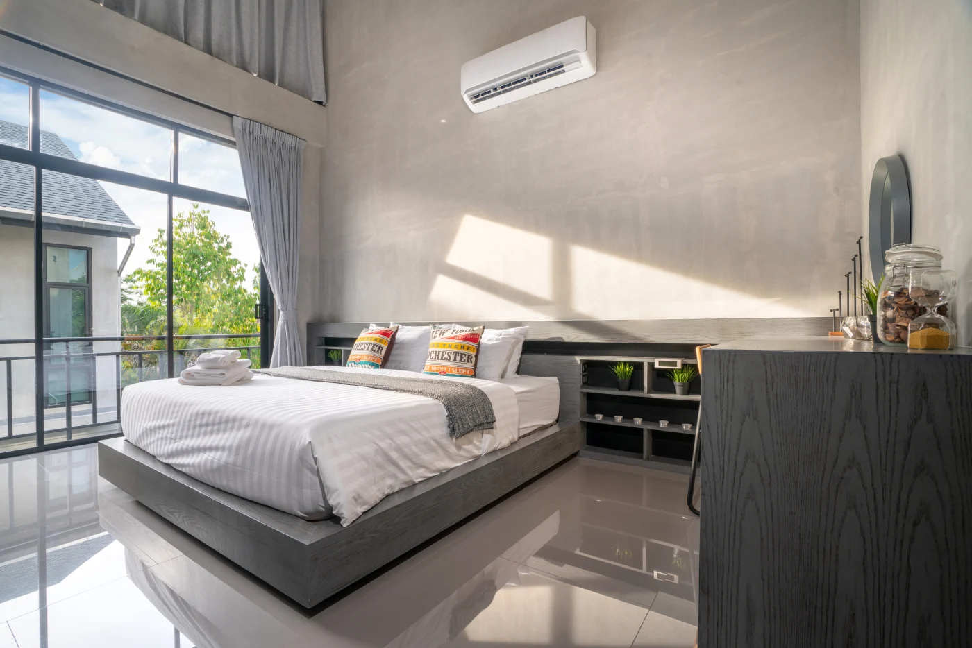 This image features a big bed in a bedroom with an AC unit above the bed on the wall near the headboard.