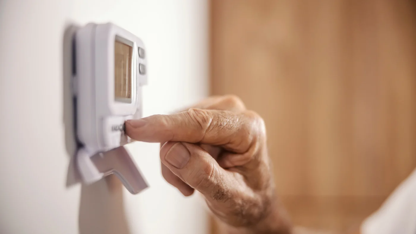 Senior’s hand adjusting thermostat on wall