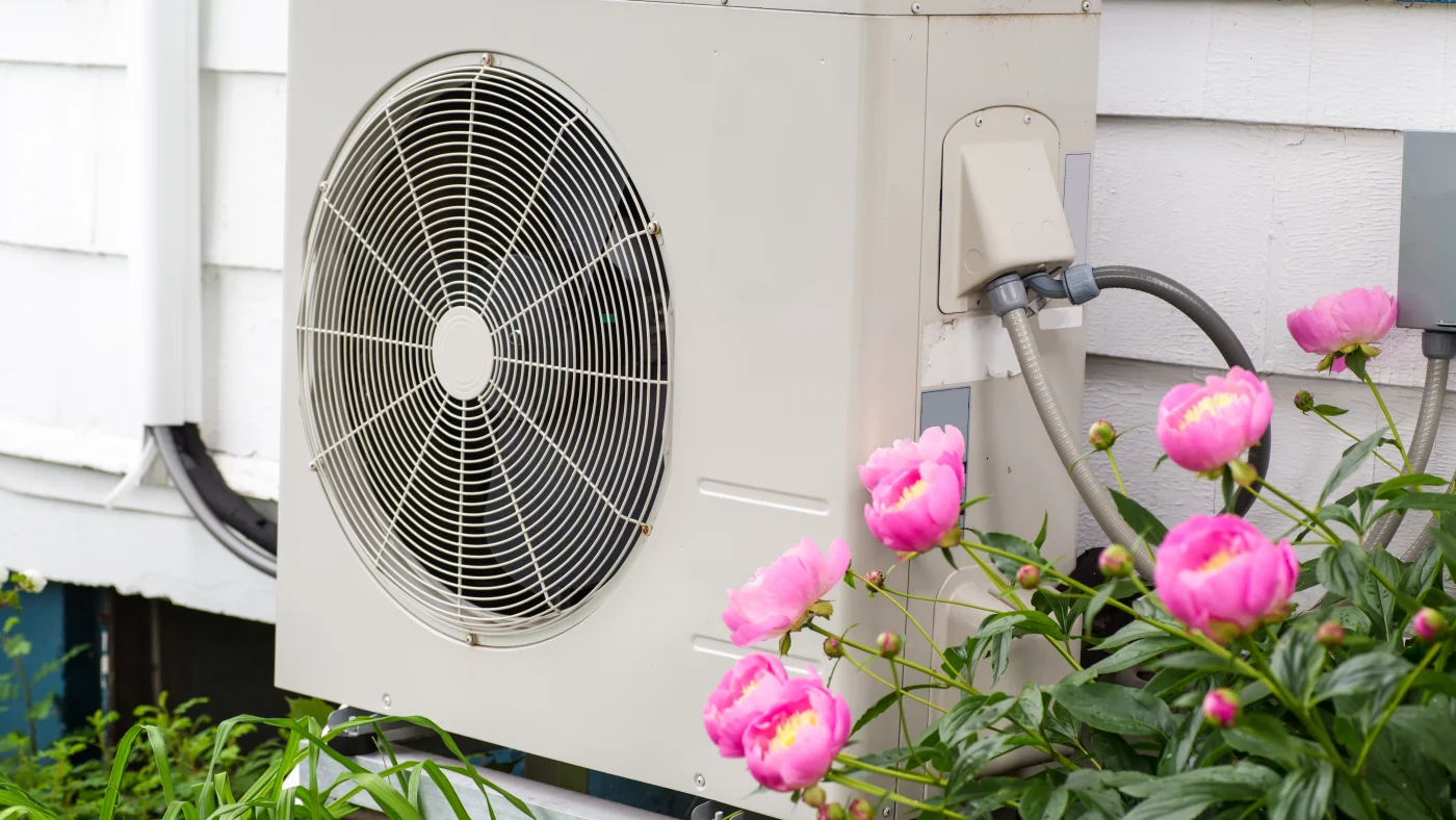 Heat pump outside of a home in garden with pink flowers