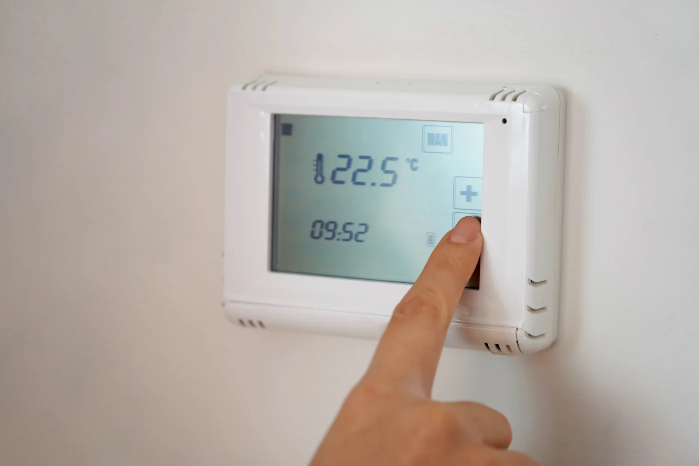 A homeowner is adjusting the thermostat on the wall