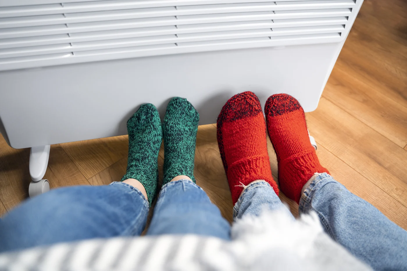 Two people are sitting in a living room with their feet near a portable heater