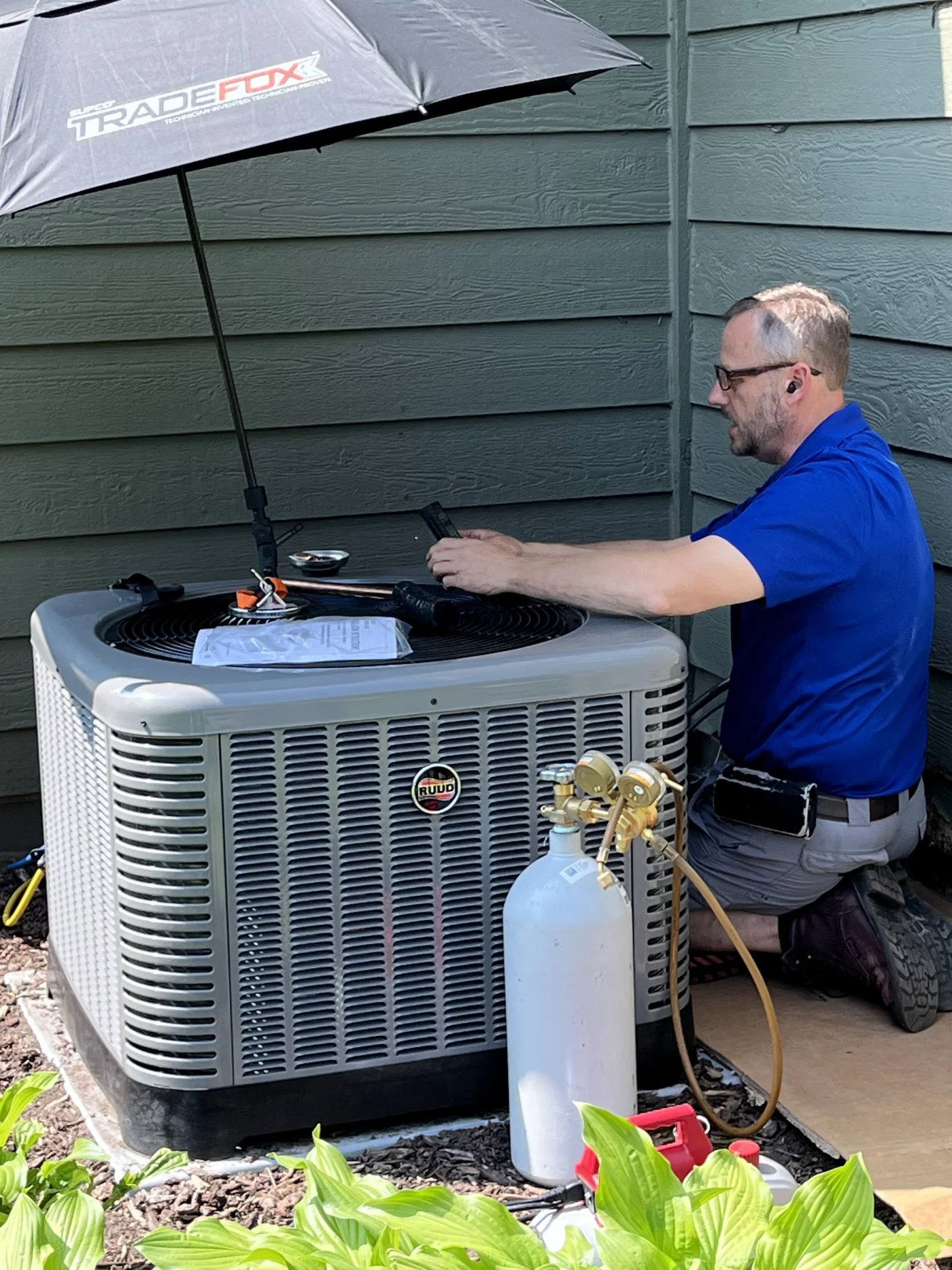 This image features a technician with a blue uniform shirt assessing an outdoor AC standard condensing unit after installing it.