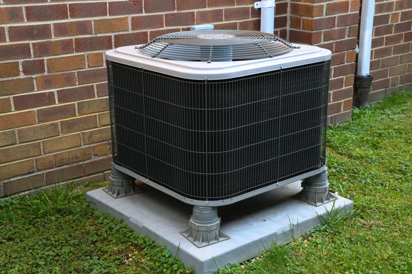 A close-up view of an outdoor central AC unit beside a brick house.
