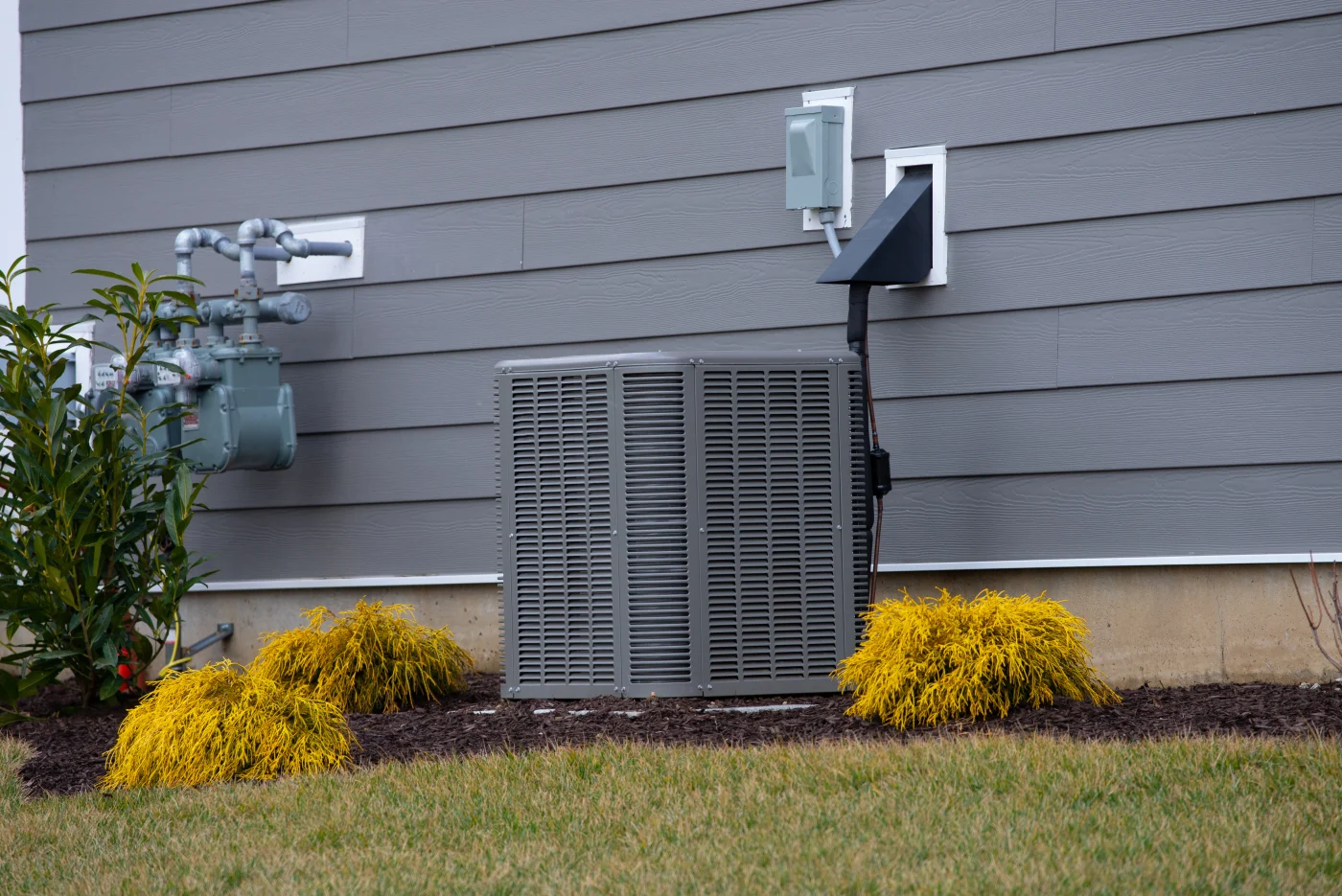 A condenser next to a home with gray siding.