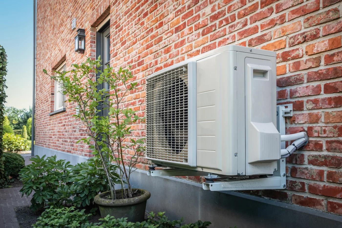 An outside unit of a heat pump installed next to a brick home.