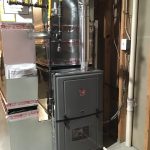 A Rheem high-efficiency gas furnace installed in a basement with connected ductwork, gas lines, and a vertical metal exhaust flue pipe.
