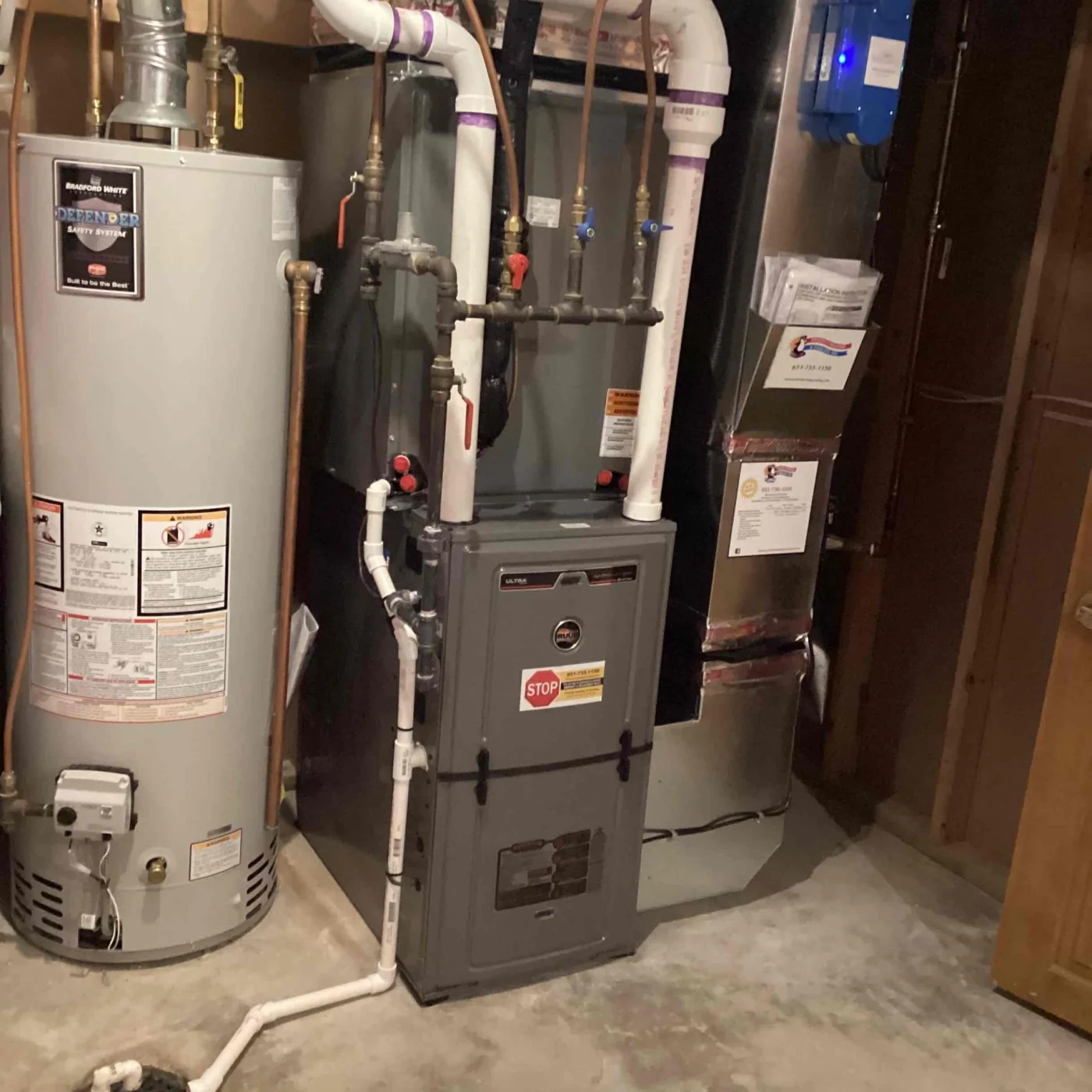 Efficient Furnace Service | Cottage Grove, MN | Priority Heating and Cooling Residential basement mechanical room showing a gray gas furnace connected to PVC vent piping beside a tall water heater.
