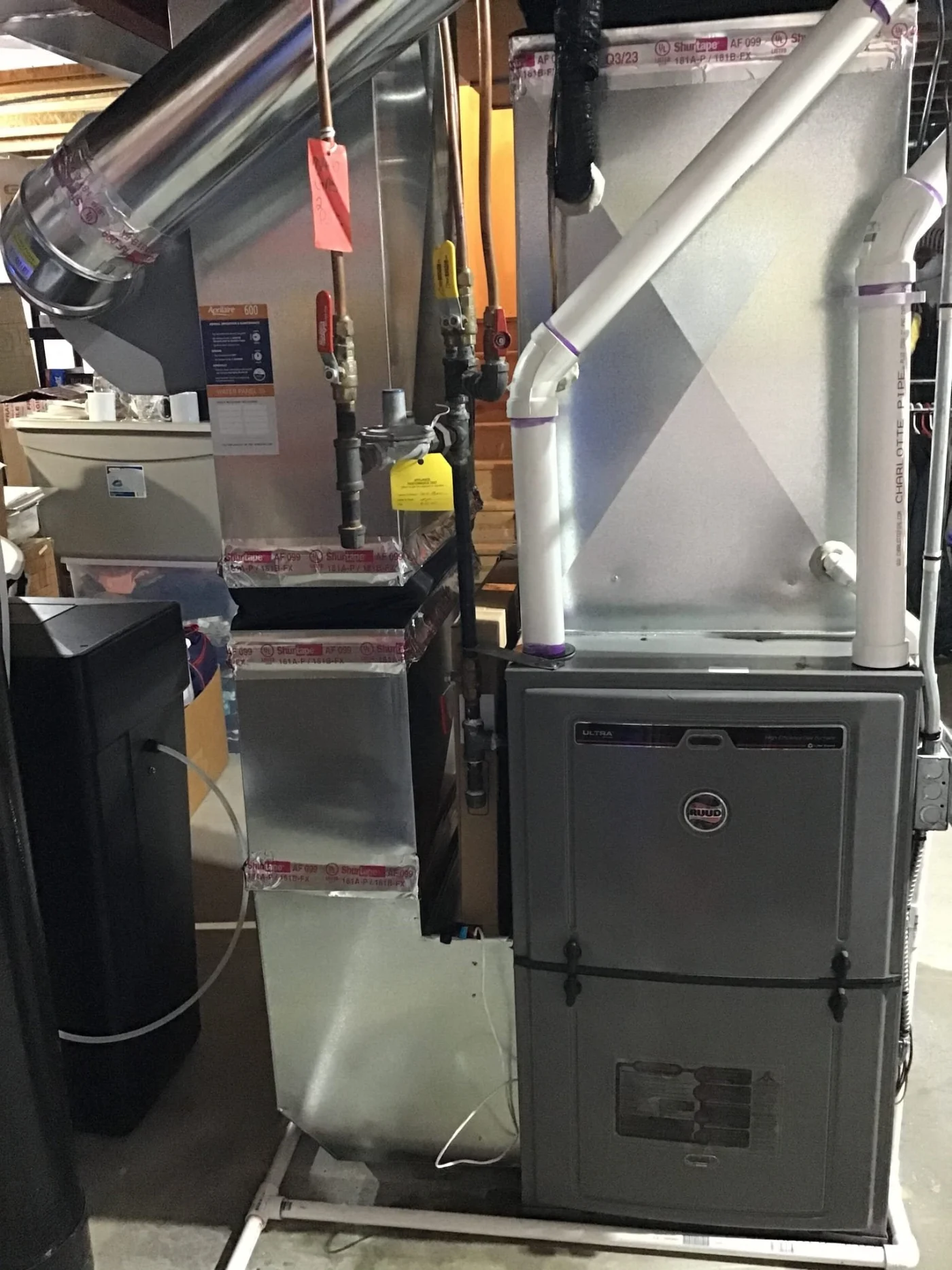 Close-up view of a residential furnace system in a basement, showing ductwork, PVC venting, and gas shutoff valves.