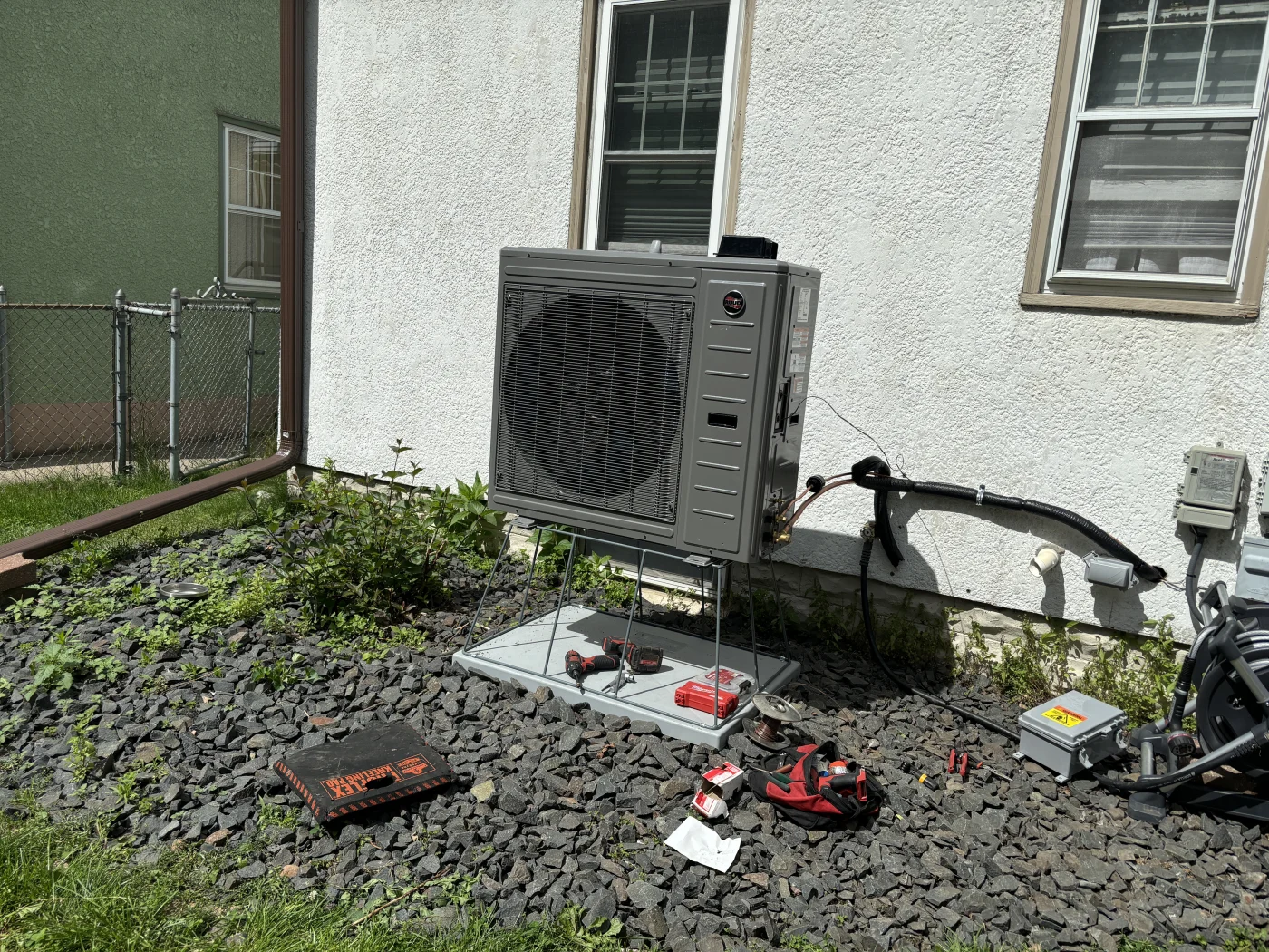 New RUUD heat pump mounted on a raised metal stand outside a home, surrounded by tools and wiring, during an in-progress installation.