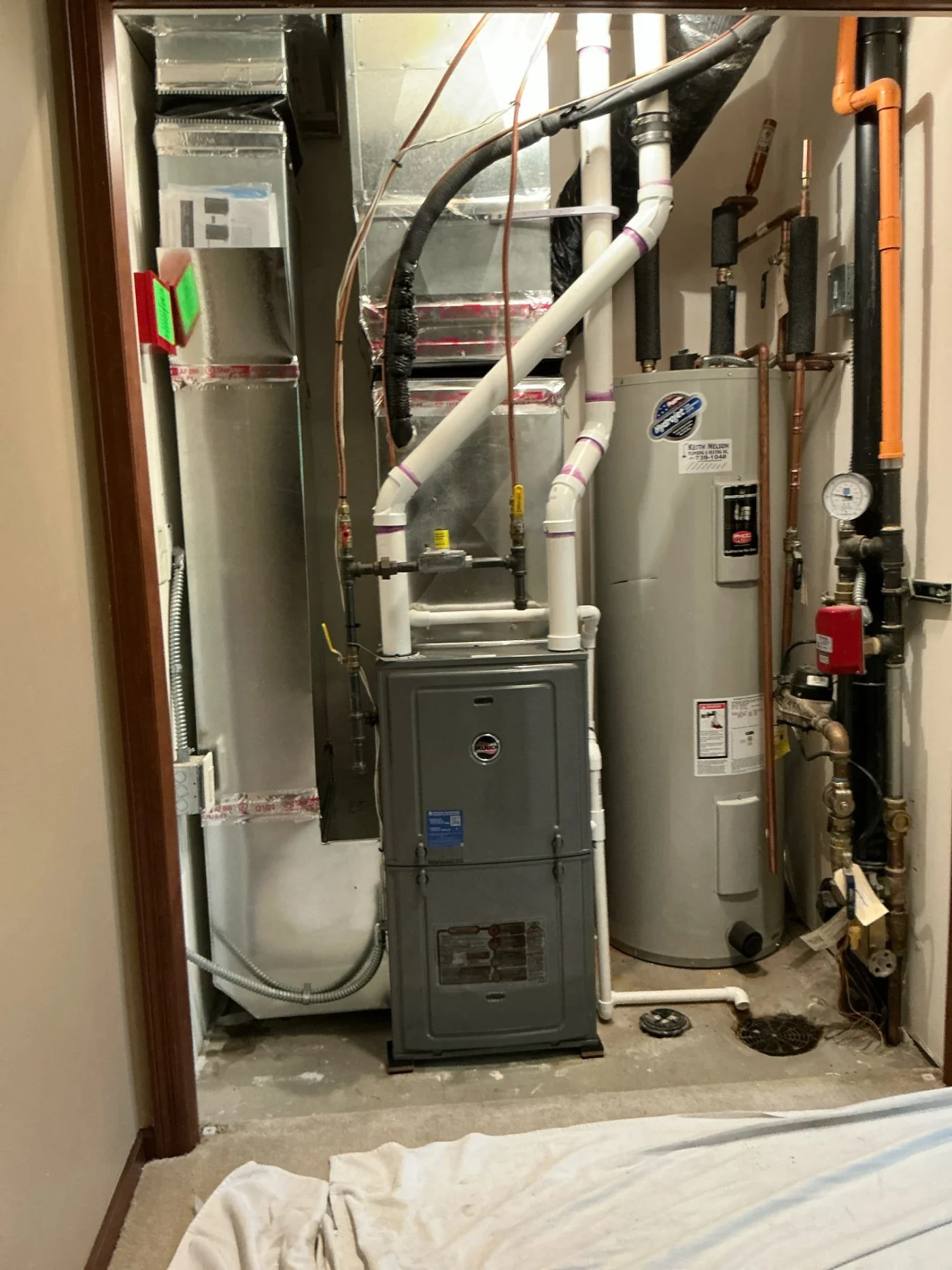 High-efficiency gas furnace and connected ductwork installed in a utility closet beside a tall water heater and plumbing lines.