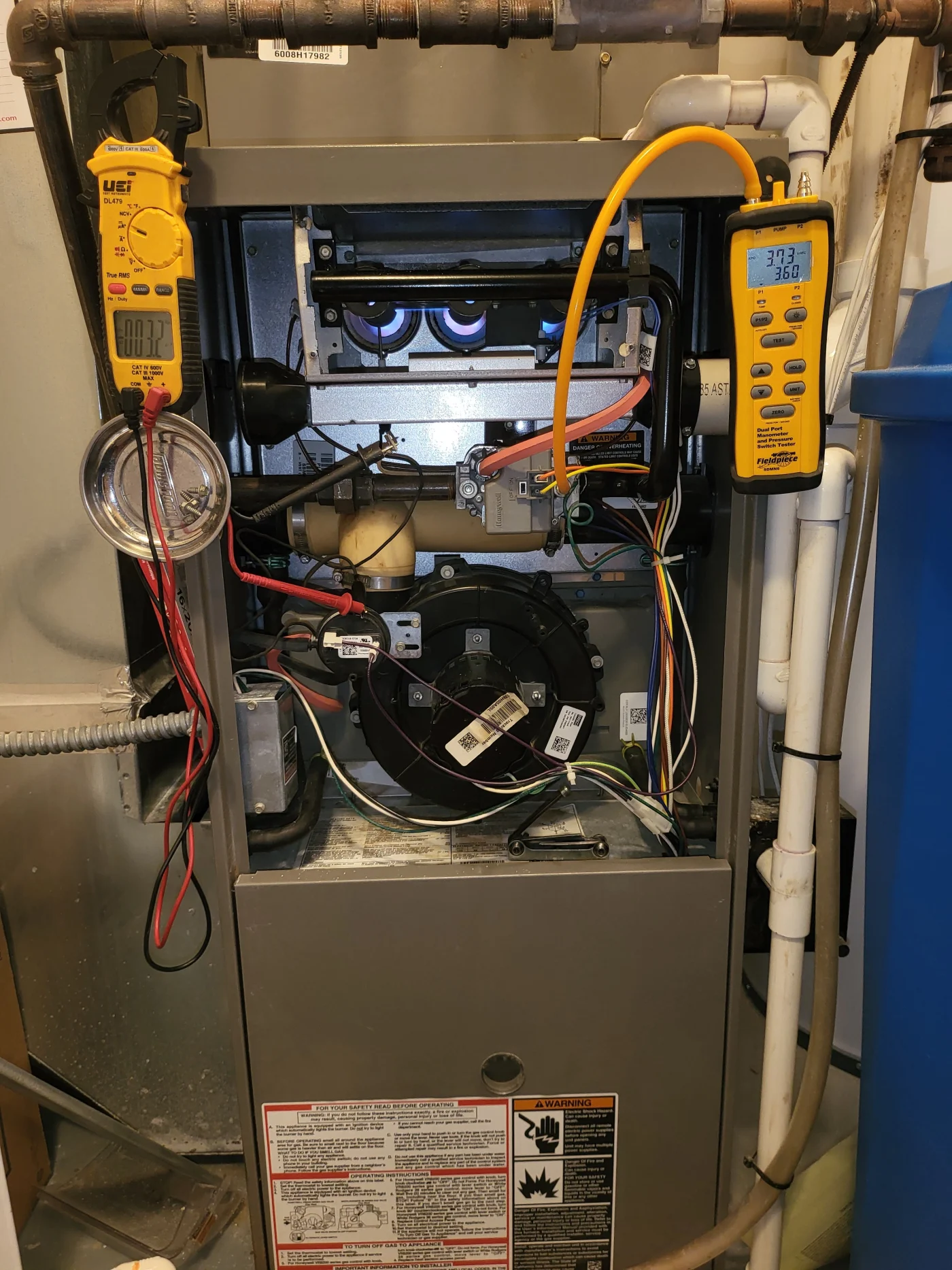 Open gas furnace with burners, wiring, and attached yellow diagnostic gauges during a professional furnace service visit.