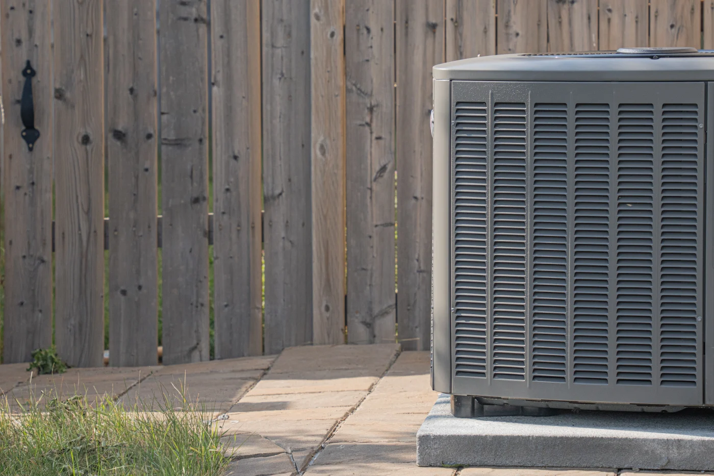 Outdoor air conditioning condenser unit on a concrete pad beside a wooden privacy fence