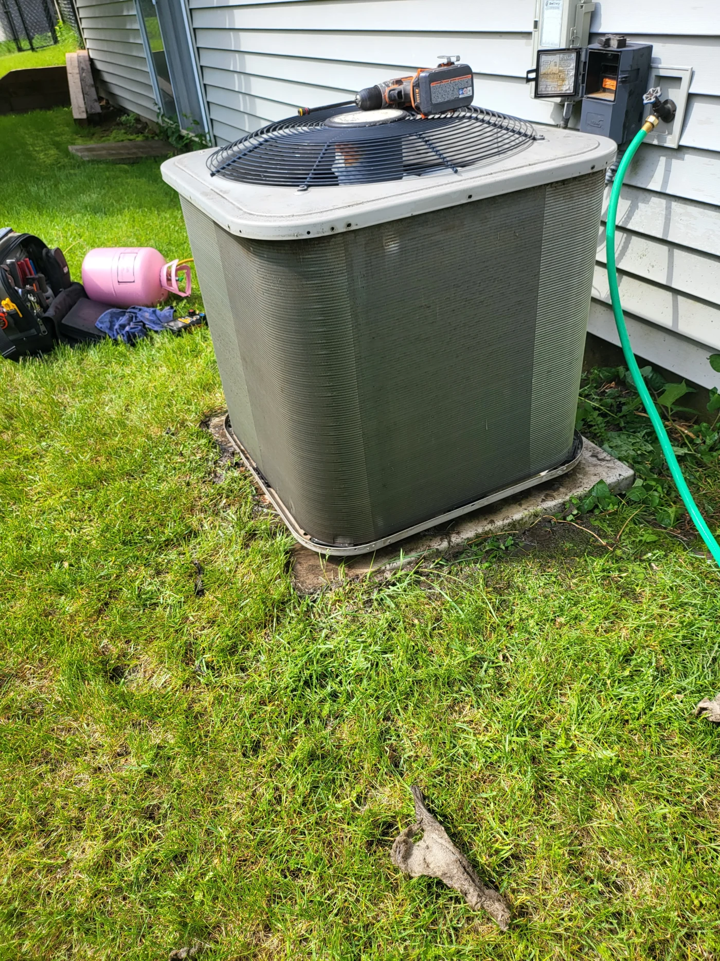 Remarkable AC Service | Maplewood, MN | Priority Heating and Cooling An outdoor air conditioner condenser unit beside a house with a cordless drill on top, a hose connected nearby.