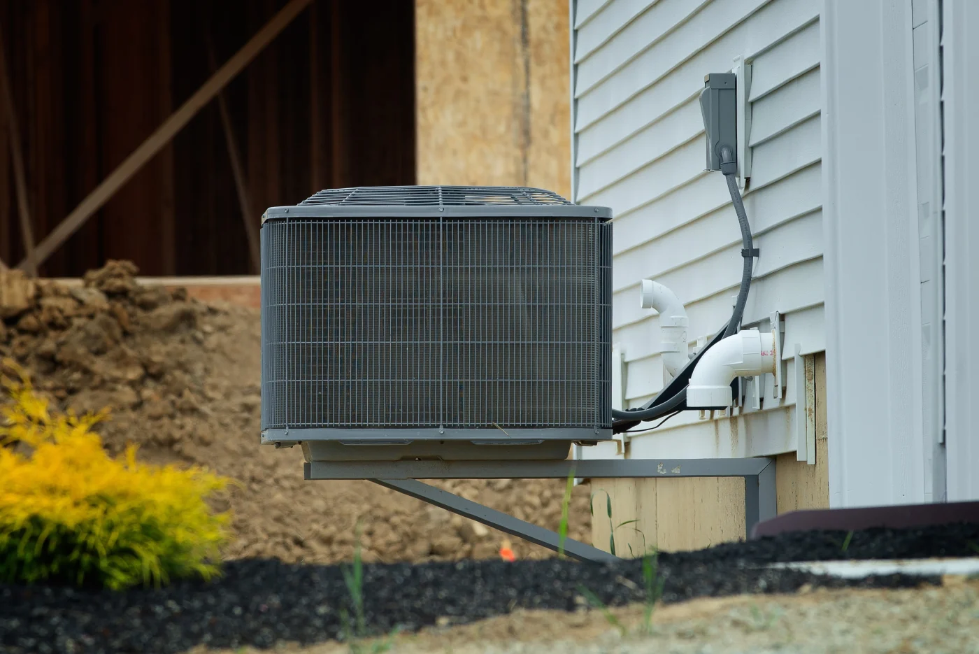 Superior AC Replacement | Lakeland, MN | Priority Heating and Cooling A wall-mounted outdoor air conditioner condenser installed beside a white-sided home, with visible electrical and drain connections.