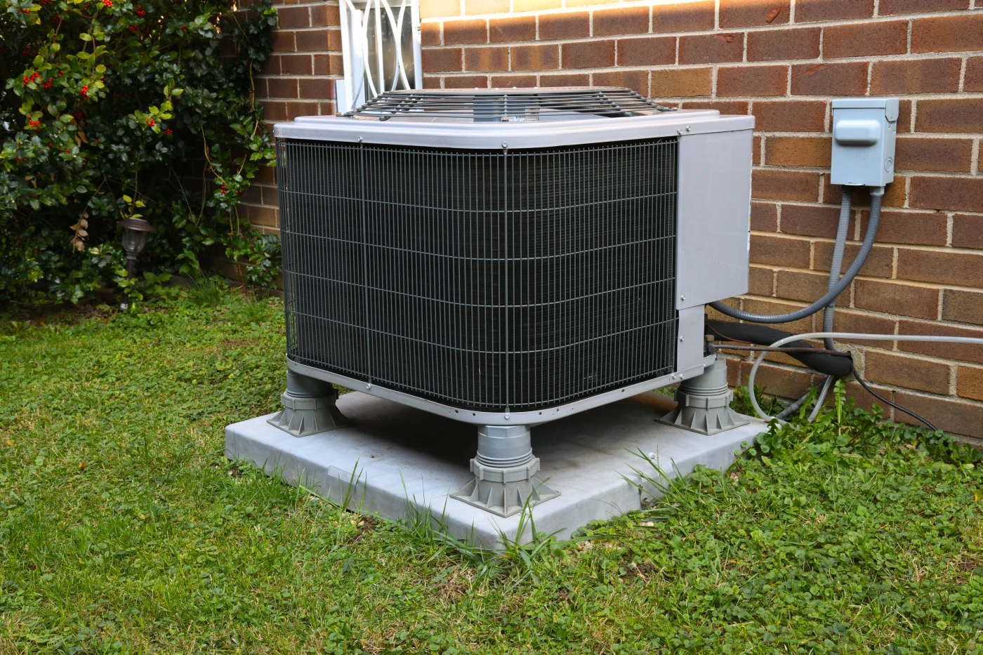 A new outdoor AC unit installed on a pad, next to a brick house.